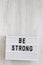 `Be strong` words on a modern board on a white wooden background, top view. Overhead, from above, flat lay. Copy space