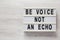 `Be voice not an echo` on a lightbox on a white wooden background, top view. Flat lay, overhead, from above. Copy space