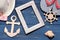 Beach accessories. A summer hat with flip flops, a wooden frame, a wooden anchor and a steering wheel on a blue background. Top vi