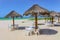 Beach bar - Tiki thatch umbrellas on sandy beach with white plastic chairs underneath and the turquioise sea and very blue sky on