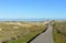 Beach with big sand dunes with vegetation and wooden boardwalk. Sunny day, morning light, Galicia, Coruna, Spain.