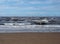 The beach at blundell sands in southport with waves braking on the beach and the wind turbines at burbo bank visible in the