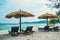 Beach calm scene with sunbeds and straw umbrellas under coconut palms close to Caribbean sea. Tropical paradise with chaise