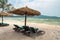 Beach calm scene with sunbeds and straw umbrellas under coconut palms close to Caribbean sea. Tropical paradise with chaise