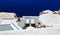 beach chairs on terrace of the hotel in Santorini, overlooking the sea, bright sun, pots of flowers, white architecture