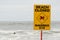 Beach closed sign and a lonely blurred surfer in the ocean.