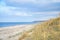 Beach crossing in Denmark by the sea. Dunes, sand water and clouds on the coast