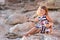 Beach cute girl posing on a rocky beach barefooted with curly hair wearing sailor dress and sun glasses