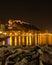 Beach at the foot of a castle with reflections of city lights in the sea