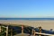 Beach with grass and wooden boardwalk with fence . Morning light, sunny day, blue sky. Galicia, Coruna, Spain.