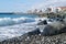 Beach with huge rocks and waves on the background of houses and water area on a Sunny day