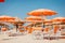 Beach in Italy. Orange umbrellas and deck chairs on the sand against the sea. Summer