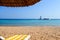 Beach lounger under a reed umbrella in front of the blue sea with a yacht