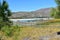 Beach with mountain, lake, wooden boardwalk and pine trees. Bright sand and turquoise water. Sunny day, blue sky, Galicia, Spain.