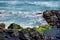 Beach near the Hanga Roa village on Easter Island, with blue waters surrounded by black volcanic rocks and green