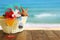 Beach objects and fruit cocktail on wooden table in front of sea landscape background
