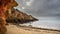 Beach and ocean landscape with high cliffs and dark sky, Algarve, Portugal