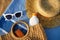 Beach scene with straw, white sunglasses, sunscreen in wicker bag on blue towel. Summer essentials for sun protection on