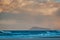 Beach scenery with blue waves, dramatic sky and mountains in the background