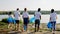 On the beach side beside the lake group of multiracial volunteers walking down the lake holding big plastic bags to