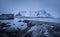 Beach with stones in blurred water, red rorbu and snowy mountains