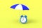 Beach striped umbrella and alarm clock on yellow background