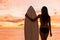 Beach sunset sexy surfer woman surfing lifestyle holding surfboard looking at ocean waves for surf. Active silhouette of