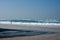 Beach surrounded by the wavy sea with a surfer near it under a blue sky and sunlight