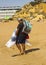 A beach trader carrying his stock of colourful fabrics along the beach in Albuferia in Portugal on a hot day