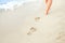 A Beach travel - woman relaxing walking on a sandy beach leaving footprints in the sand. Close up detail of female feet on golden