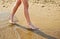 Beach travel - young girl walking on sand beach leaving footprints in the sand. Closeup detail of female feet and golden sand