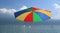 Beach umbrella in rainbow colors and group of windsurfers on gar