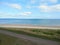 Beach view from yard, small road behind fence and white fluffy clouds on blue sky