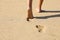 Beach woman legs feet walking barefoot on sand leaving footprints on golden sand in sunset. Vacation travel freedom people