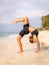 Beach yoga. Young woman practicing Eka Pada Chakrasana, One Legged Wheel Pose. Upward facing bow pose is a deep backbend.