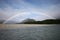 Beachfront with full rainbow on shore framing mountain in sunny blue sky