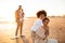 Beachside bonds. Mother and son embracing and smiling at camera, father with little son standing on background