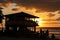 beachside eatery, with view of sunset over the ocean, and silhouettes of people on the sand