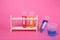 Beakers and test tubes with colorful liquids in wooden stand on bright pink background. Kids chemical experiment set