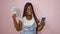 Beaming african american woman flaunting dollar bills with phone over pink isolated background - a winner in online betting