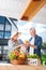 Beaming bearded man taking fresh orange out of basket standing near wife