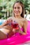 Beaming woman lying on air mattress in the pool holding cold drink