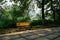 Beams of summer morning sunlight on shady wayside bench near riv