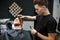 Beard grooming. Side view of young bearded man getting beard haircut by hairdresser while sitting in chair at barbershop
