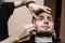 Beard haircut in a barbershop, a young guy shaving his beard with a razor, close-up