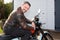 Beard man in brown leather motorbike fashion jacket sit on vintage retro motorcycle outdoors