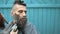 Beard styling with electric trimmer. Barber hand cutting beard with clipper and comb at outdoor barbershop