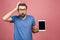 Bearded amazed man in eyeglasses which showing blank tablet computer screen and looking at camera. Isolated over pink background