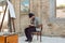 Bearded artist, similar to the popular Niko Pirosmani, drawing paintings at the easel during the weekend