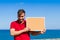 Bearded attractive inviting young man holding a framed blank corkboard in blue sky